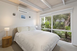 Een slaapkamer met een groot bed, een raam met uitzicht op groen en een airconditioner aan de muur.
