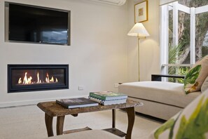 Una sala de estar con chimenea, un sofá, una mesa de centro con libros y una lámpara.