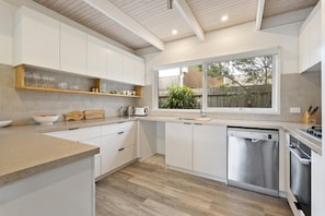 Una cocina moderna con armarios blancos, lavavajillas integrado y ventana con vista a zonas verdes.