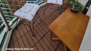 Ein Balkon mit Korbstühlen und einem Tisch, der auf einen Stadtblick blickt.