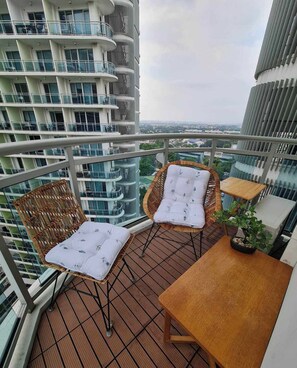 Un balcon avec des fauteuils et une table en osier, offrant une vue sur le paysage urbain.
