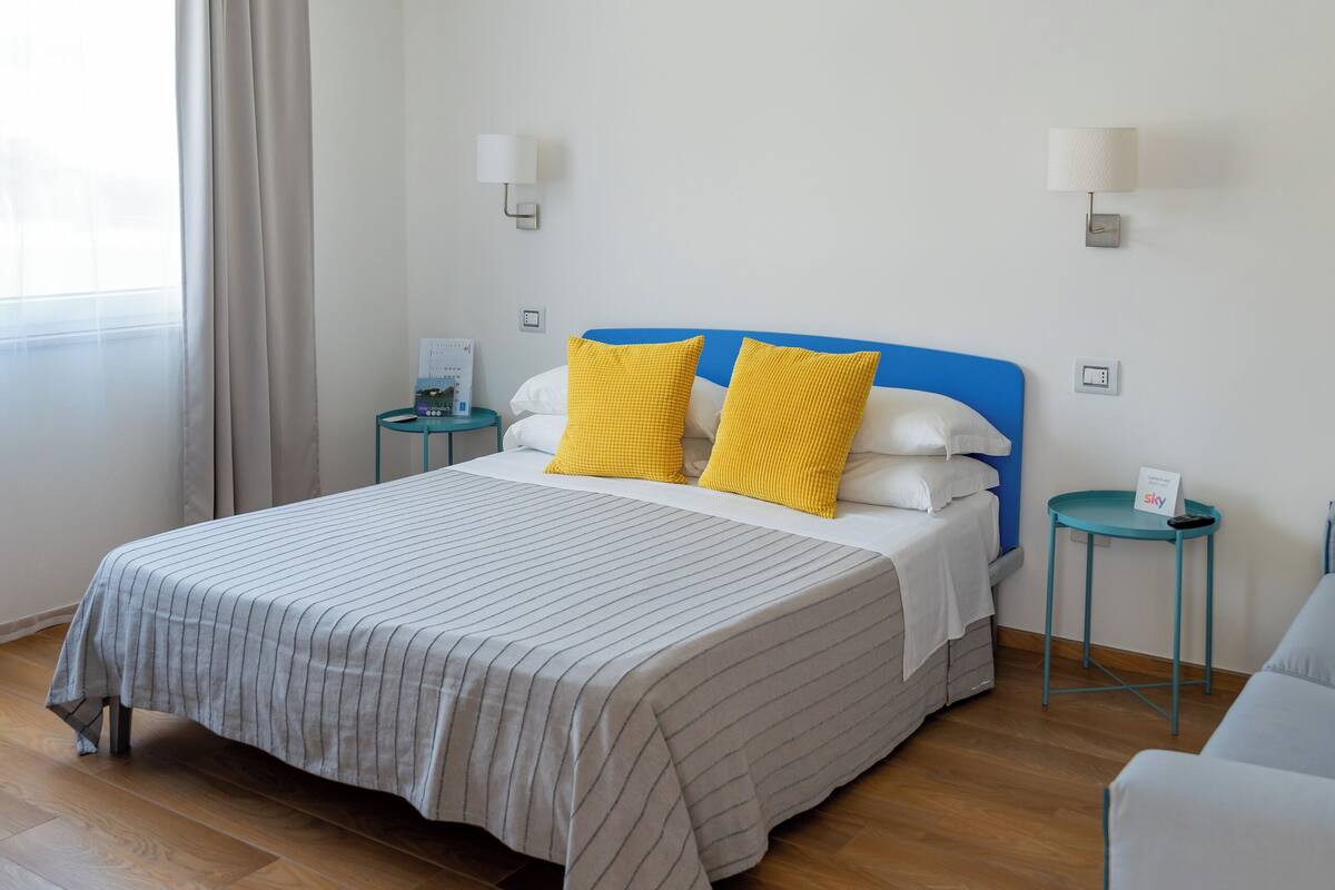 A hotel room with a bed, two bedside tables, a nightstand, a chair, and a window with curtains.