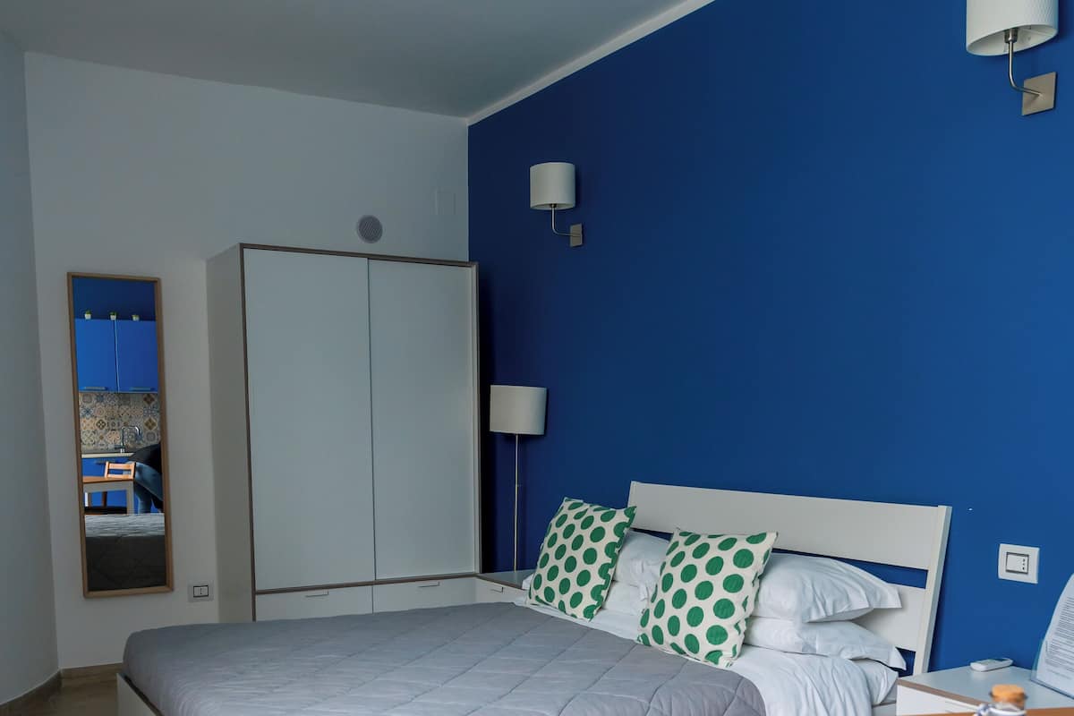 A bedroom with a bed, a wooden chair, a table, a wardrobe, and a mirror.