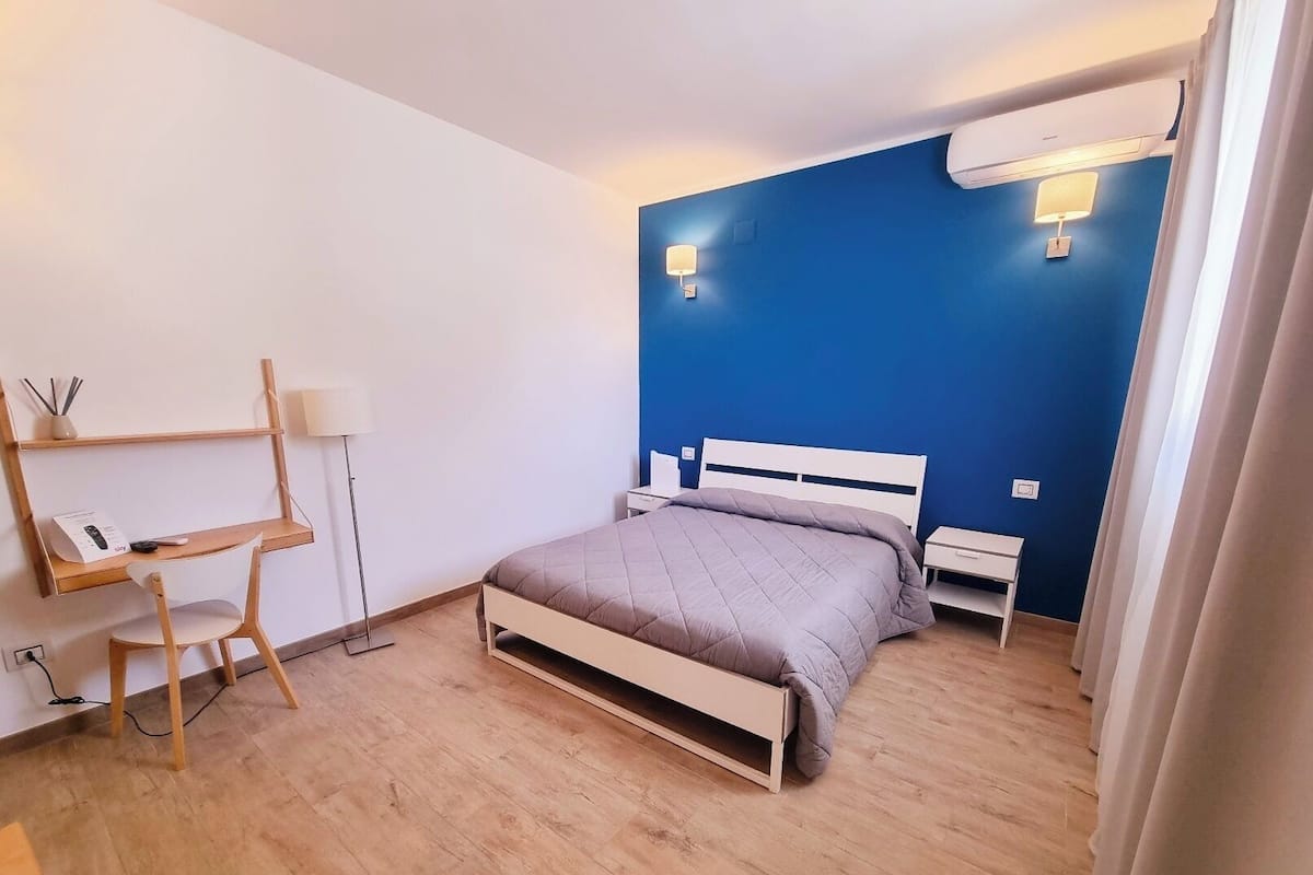 A bedroom with a bed, bedside tables, a desk with a chair, and a lamp.