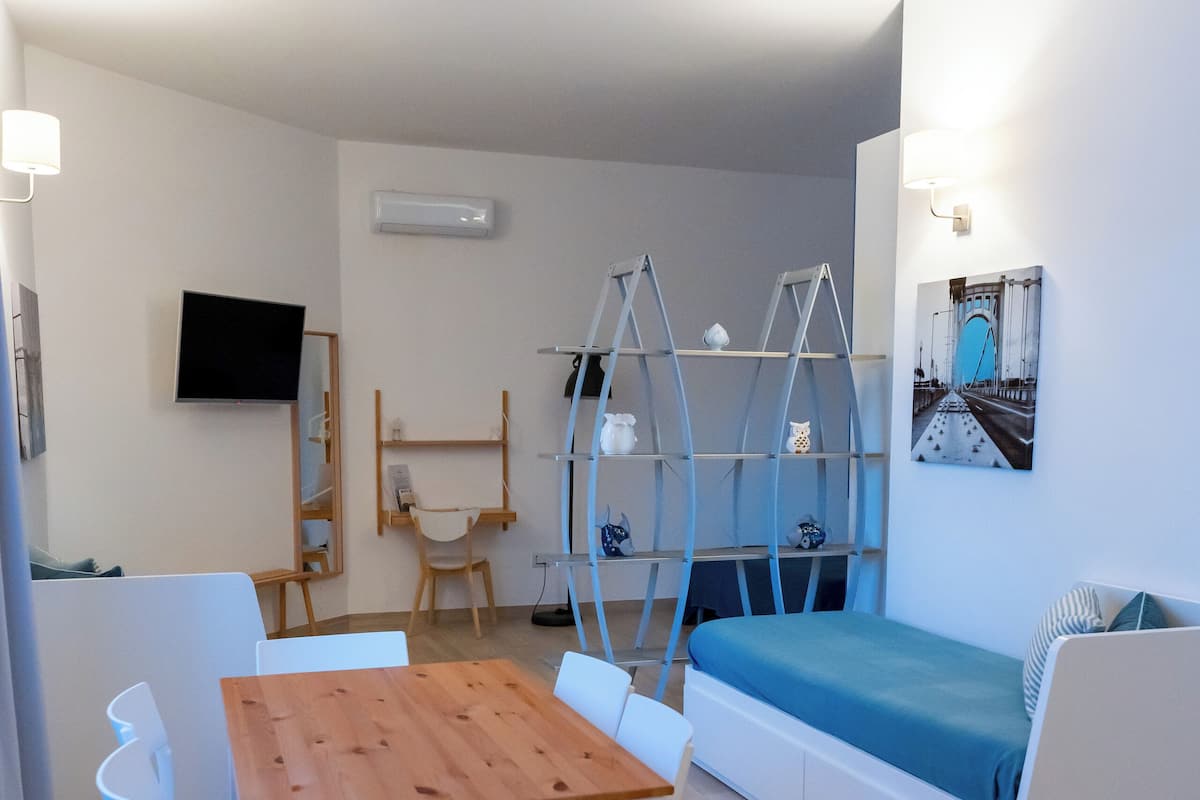 A modern living room with a wooden dining table, white chairs, a sofa, and a TV mounted on the wall.