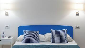 A hotel room with a bed, two pillows, a nightstand, and a wall-mounted lamp.