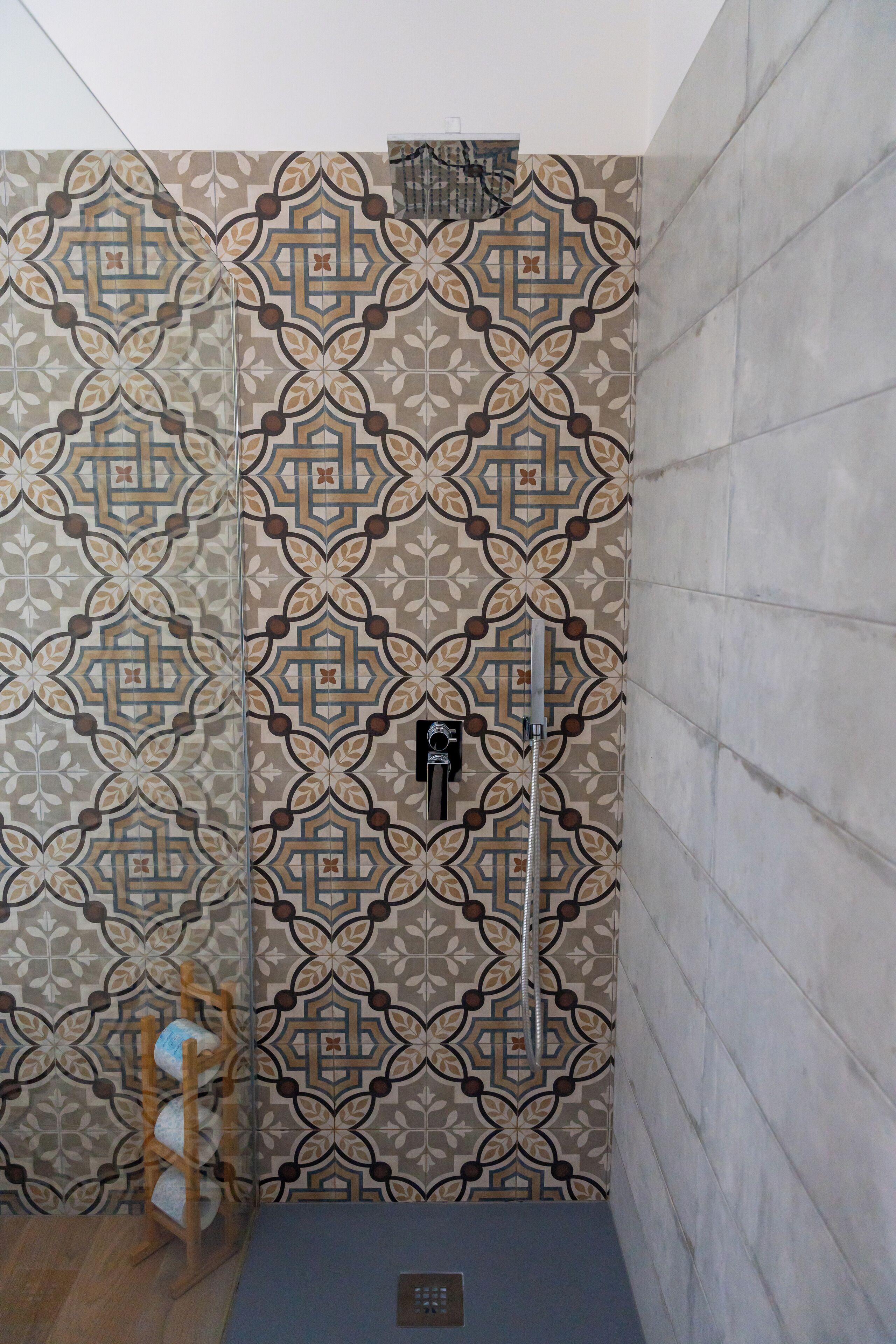 Une salle de bain avec des carreaux décorés, une chaise en bois et un élément en métal fixé au mur.