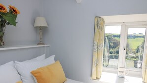 Ein Schlafzimmer mit einem Bett, Kissen, einer Lampe, einer Vase mit Blumen und einem Fenster mit Vorhängen.