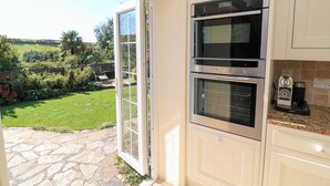 Eine Küche mit zwei Backöfen, einer Kaffeemaschine und Blick auf einen Garten durch eine offene Tür.