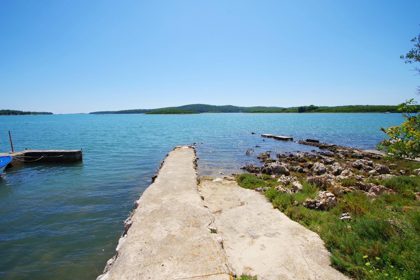A concrete pier extending into a calm lake with a small boat docked on the left.