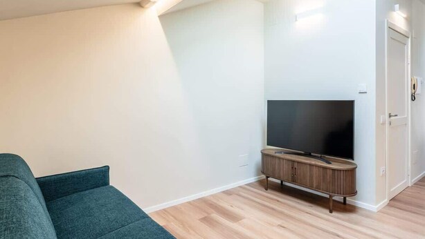 A modern living room with a flat-screen TV, a wooden cabinet, and a teal sofa. - Mansarda Norina - Affitti Brevi Italia (Lucca)