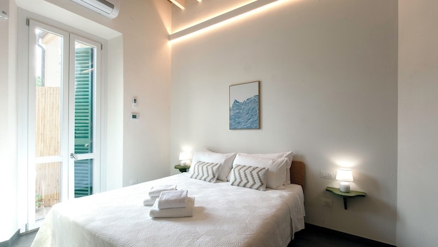 Ein Schlafzimmer mit einem Bett, zwei Nachttischlampen, einem Wandbild und einem Fenster mit Rollläden.