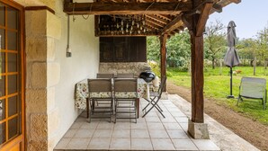 Une terrasse extérieure dotée d’une pergola en bois, d’une table avec des chaises, d’un barbecue et offrant une vue sur un jardin.