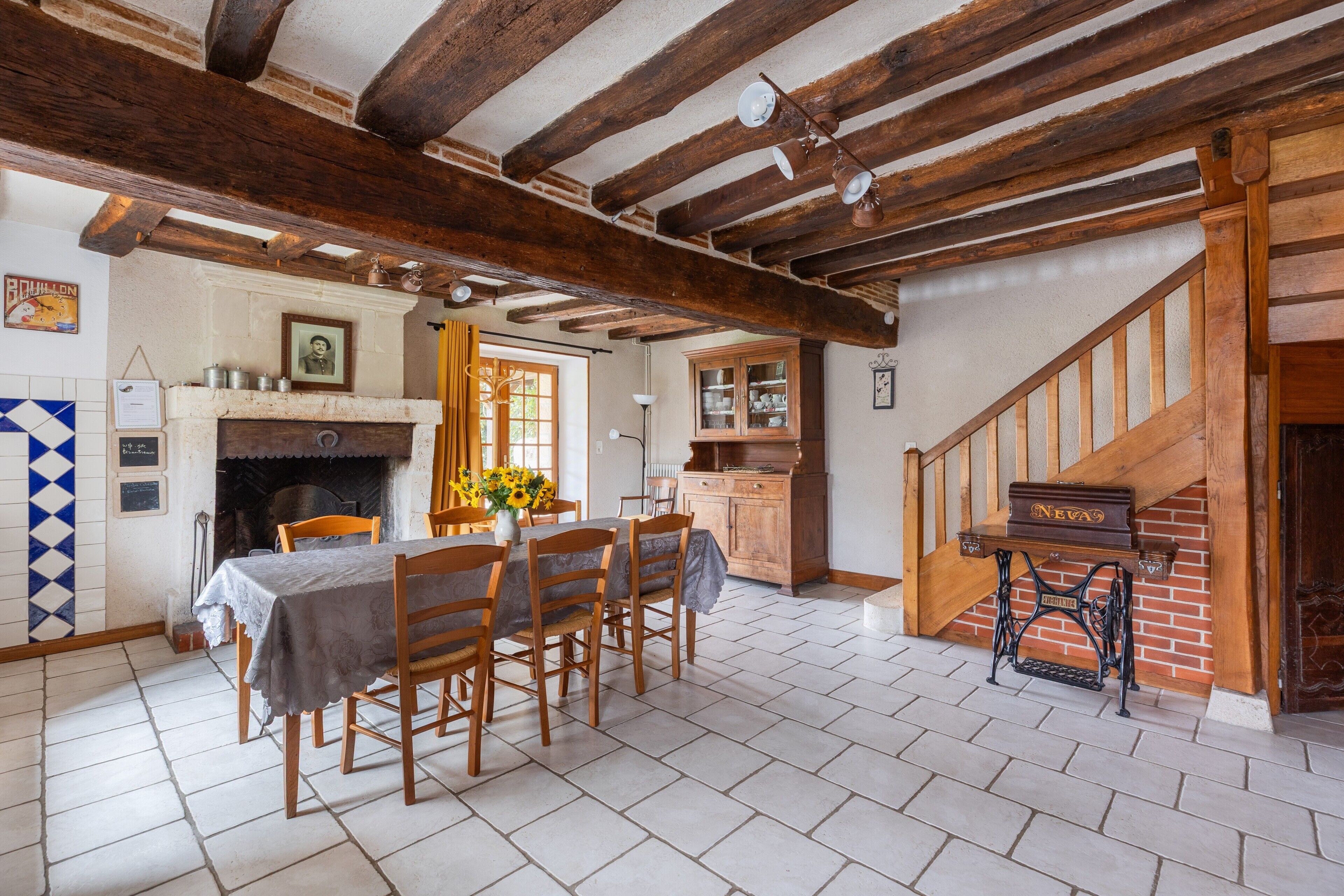A dining area with a table set for four, a fireplace, and a staircase leading to an upper level.