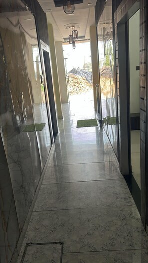 A corridor with marble flooring, glass doors, and a view of an outdoor area with construction materials. - Hotel Sultan Paradise (Roorkee)