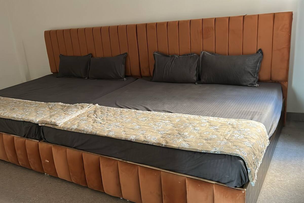 A bed with a wooden headboard, grey bedding, and a patterned throw blanket.