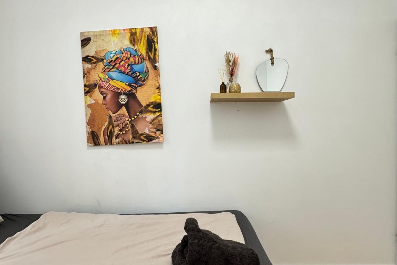 Ein Bett mit einer beigen Bettdecke, ein Wandbild einer Person in traditioneller Tracht und ein kleines Regal mit Dekorationen.