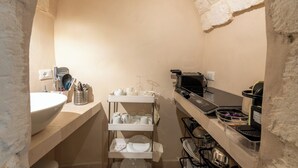 A narrow kitchen with a white sink, a metal rack with dishes, and a coffee machine.