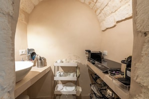A compact kitchen with a white sink, a metal rack with dishes, a coffee machine, and a microwave.