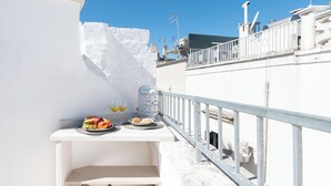 A rooftop terrace with a white table set with fruits, glasses of juice, and a decorative vase.