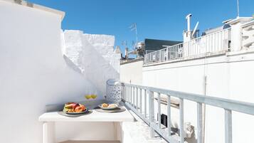 Una terrazza sul tetto con un tavolo bianco apparecchiato con frutta, bicchieri di succo e un vaso decorativo.