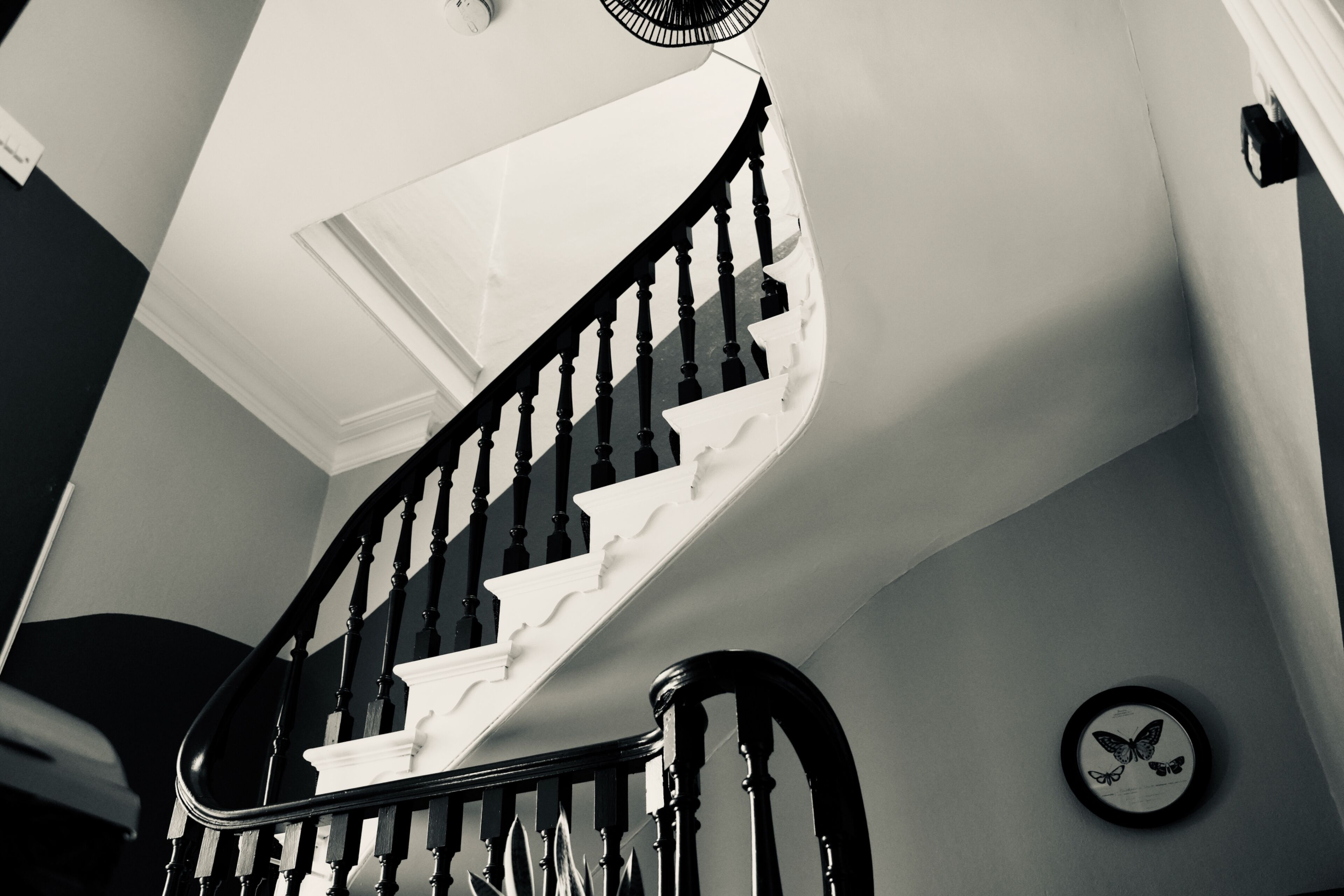 Eine Treppe mit schwarzer Handlauf und weißen Stufen, die zu einer Zwischenebene mit einer an der Wand befestigten Uhr führt.