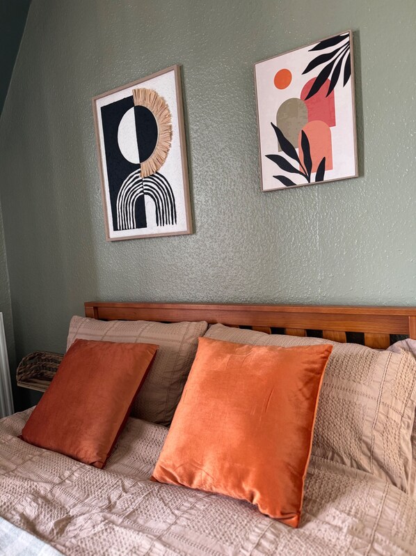En säng med en sänggavel, två orange kuddar och två inramade konstverk på väggen.
