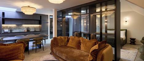 A modern living room with a large brown sofa, a dining area, and a kitchen with a marble backsplash.