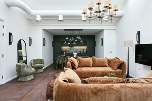 A modern living room with a brown sofa, green armchairs, and a dining area with a dark-colored table and chairs.