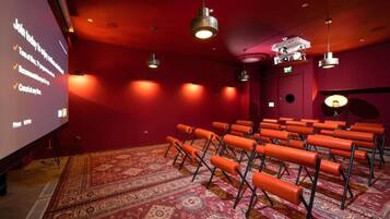 Une salle de théâtre avec des rangées de sièges orange, un grand écran et des murs rouges.