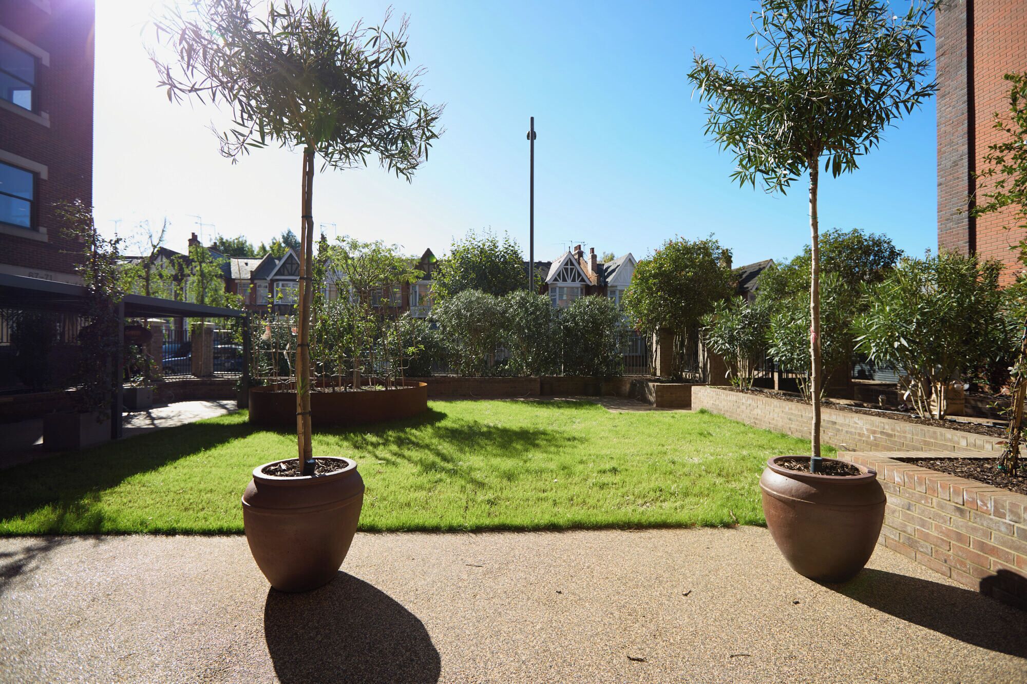 A courtyard with two large terracotta planters, a grassy lawn, and a brick wall.