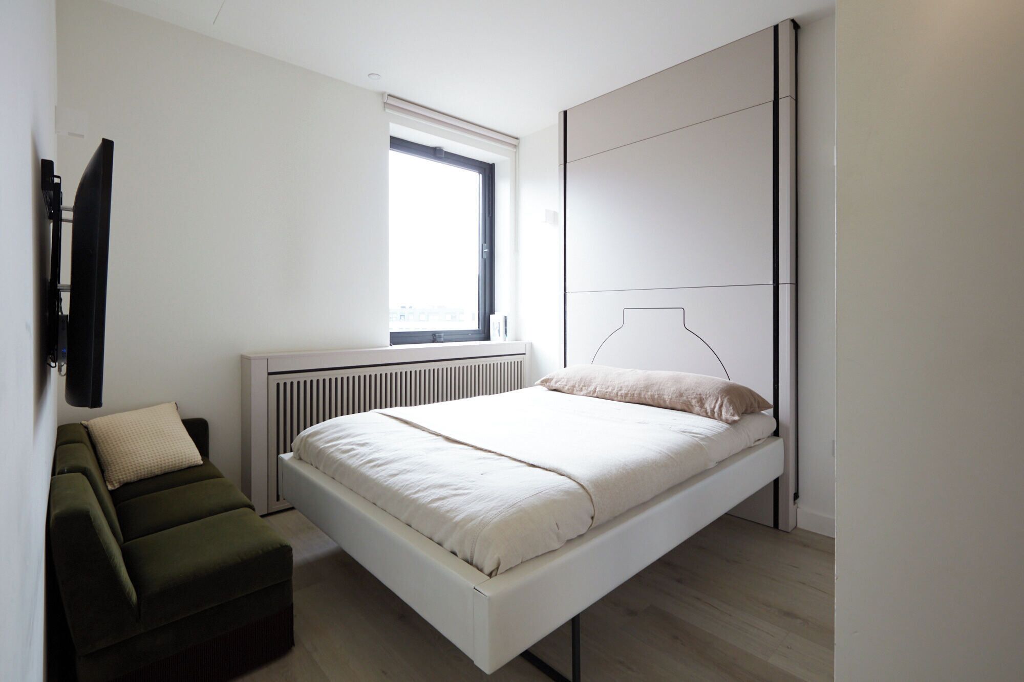 A modern bedroom with a bed, a window, a radiator, and a green chair.