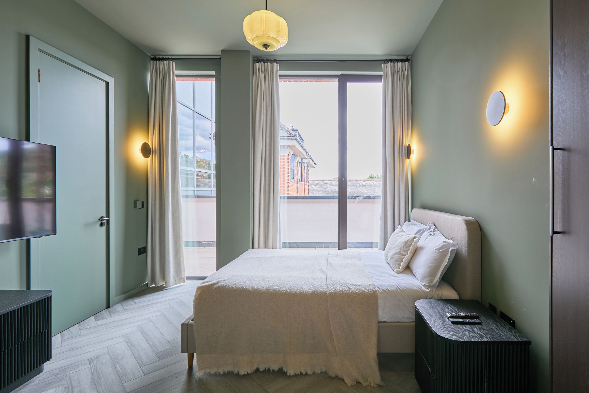 A modern bedroom with a bed, a TV, a bedside table, and a window with curtains.