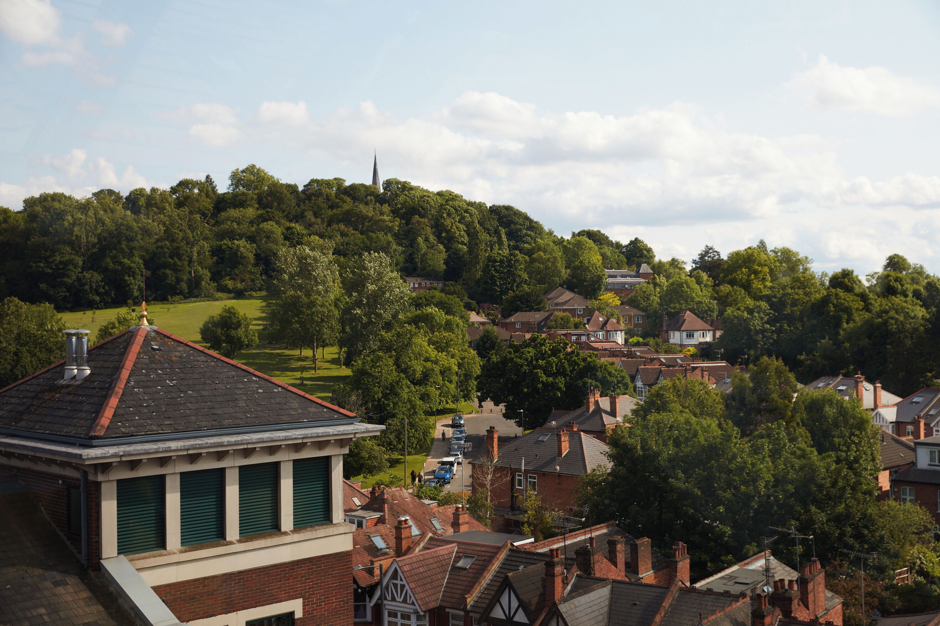 A residential area with houses, a church spire, and a green hill in the background.