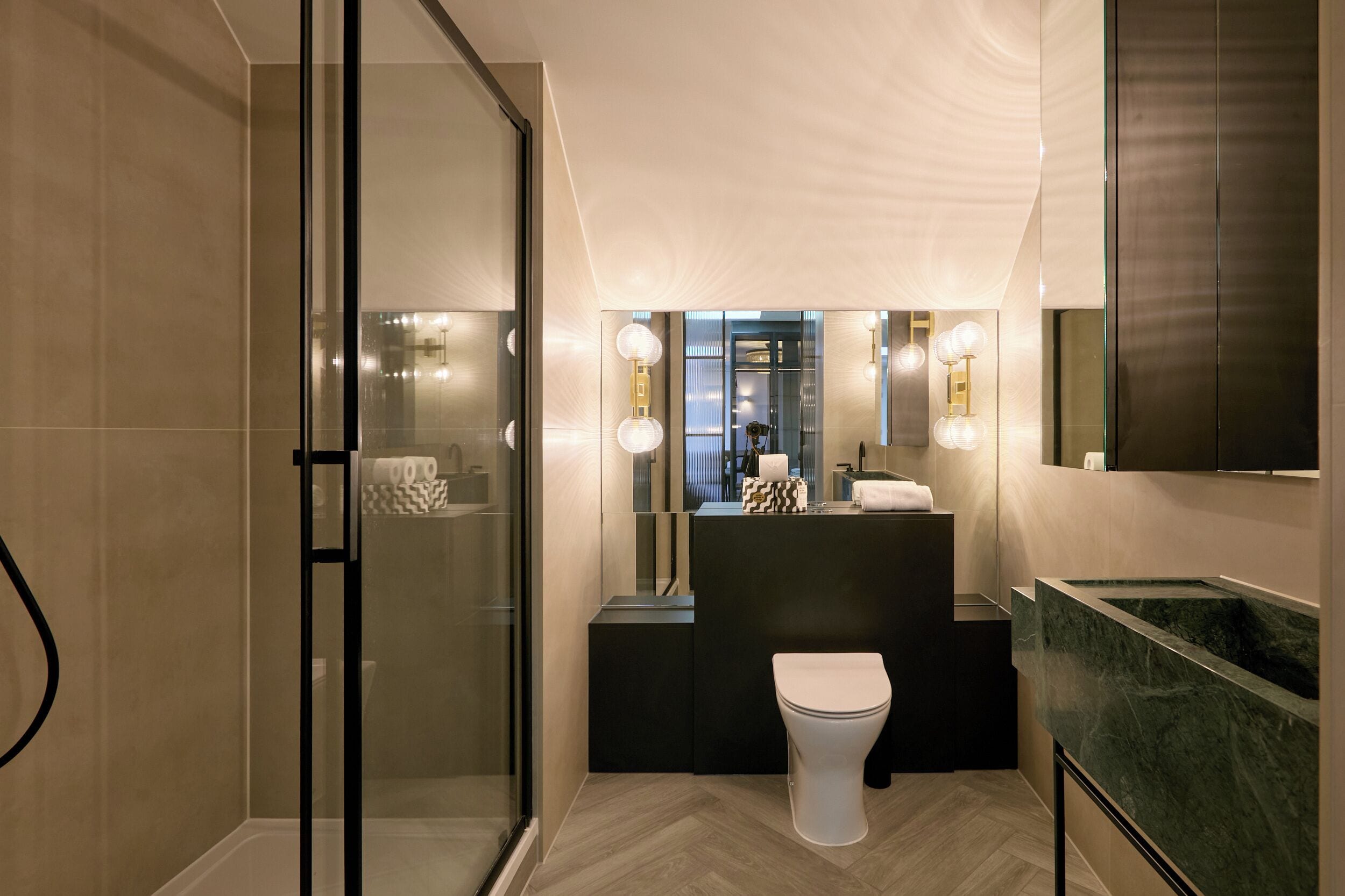 Un baño moderno con cabina de ducha de vidrio, tocador negro y encimera de mármol, y un inodoro blanco.