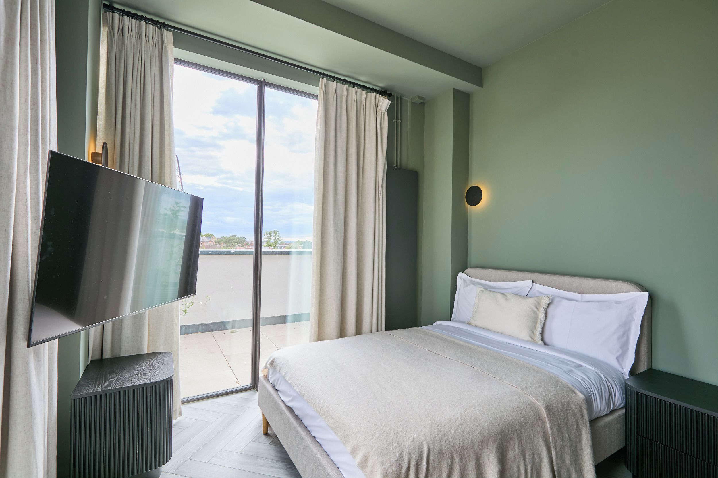 Hotellihuone, jossa on sänky, televisio, ikkuna verhoilla ja näkymä ulos.