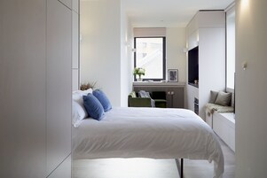 Un dormitorio moderno con una cama grande, un sillón verde y una ventana con vistas a edificios.