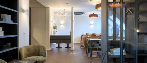 A modern interior with a herringbone wood floor, a sofa, a dining area, and a glass partitioned room with a bed.