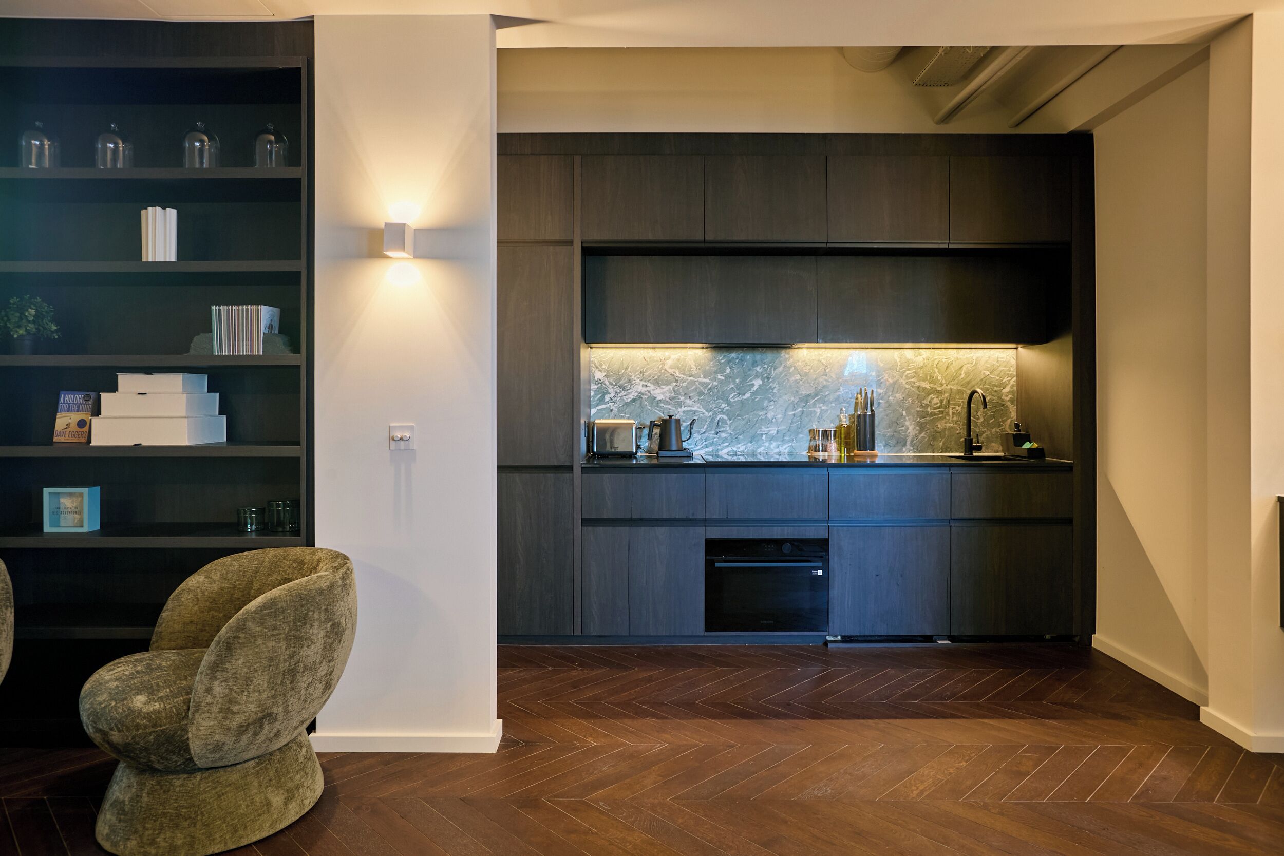 Una cucina moderna con pensili in legno scuro, zoccolo in marmo e forno incassato.