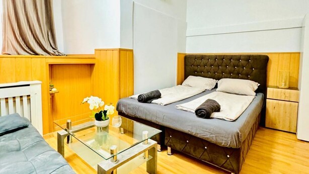 A bedroom with a bed, a glass table with a vase, and a wooden headboard.