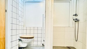 A bathroom with a toilet, shower, and a window.