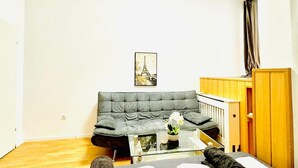 A living room with a grey sofa, a glass coffee table, a picture of the Eiffel Tower, and a wooden cabinet.