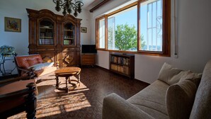 A living room with a large window, a wooden cabinet, a leather sofa, and a wooden table. - Villa Camilla App Garden (Diano Castello)