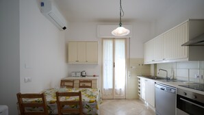 A compact kitchen with a dining area, white cabinetry, a dishwasher, and a small table with chairs. - Villa Camilla App Garden (Diano Castello)