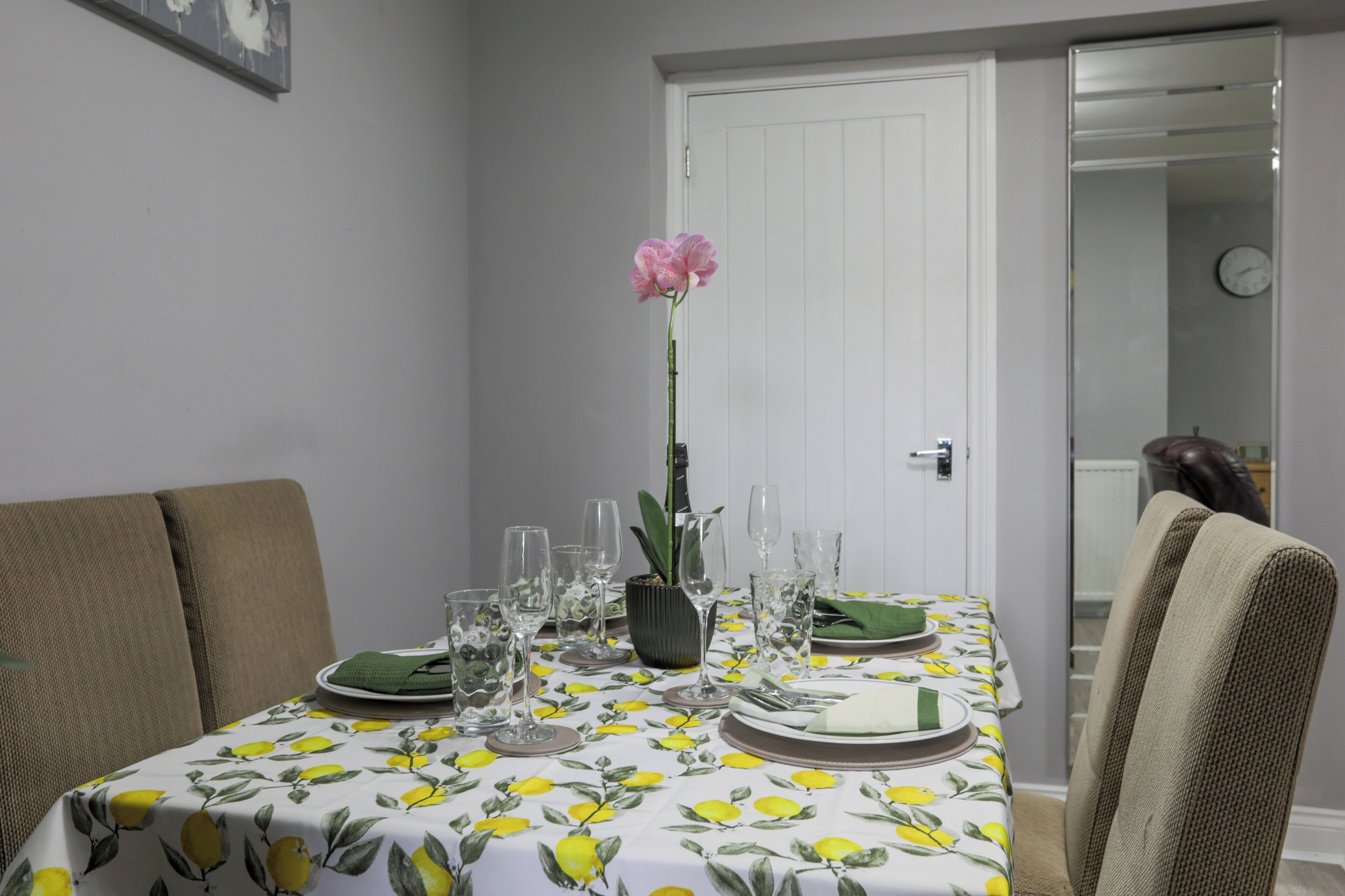 Une table à manger dressée avec des assiettes, des verres et un vase contenant une fleur rose.