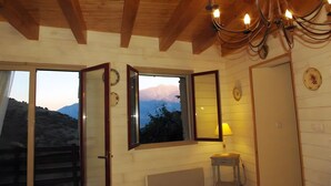 A wooden interior with a chandelier, a window with a mountain view, and a door. - Gîte Madres Coronat Balcon du Canigou (Jujols)
