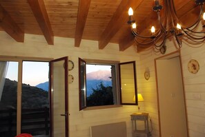 A wooden interior with a chandelier, a window with a mountain view, and a door. - Gîte Madres Coronat Balcon du Canigou (Jujols)
