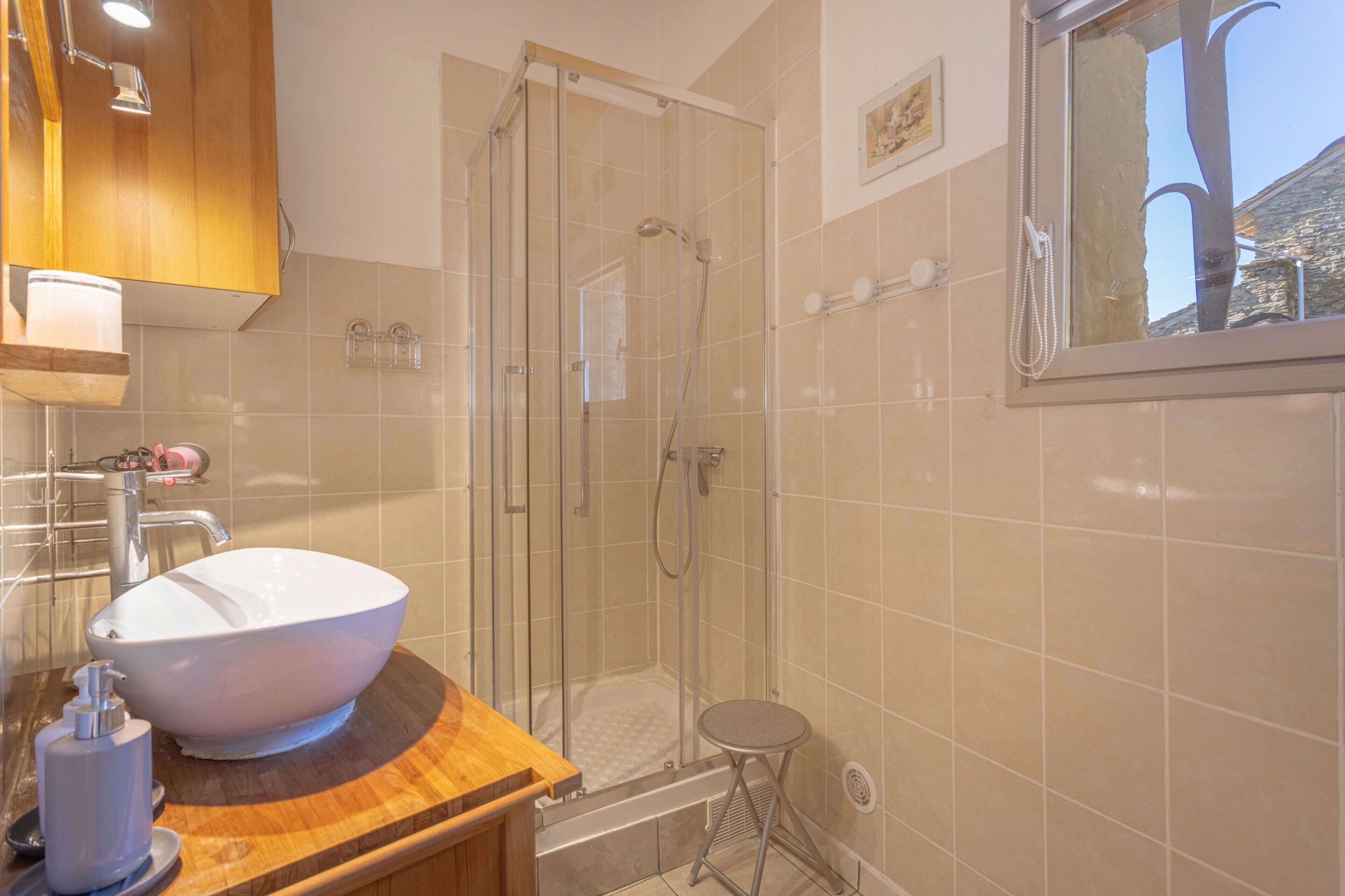 Een badkamer met een grote witte wasbak, een douche met glazen wanden en een houten wastafelmeubel.
