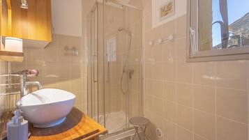 Een badkamer met een grote witte wasbak, een douche met glazen wanden en een houten wastafelmeubel.