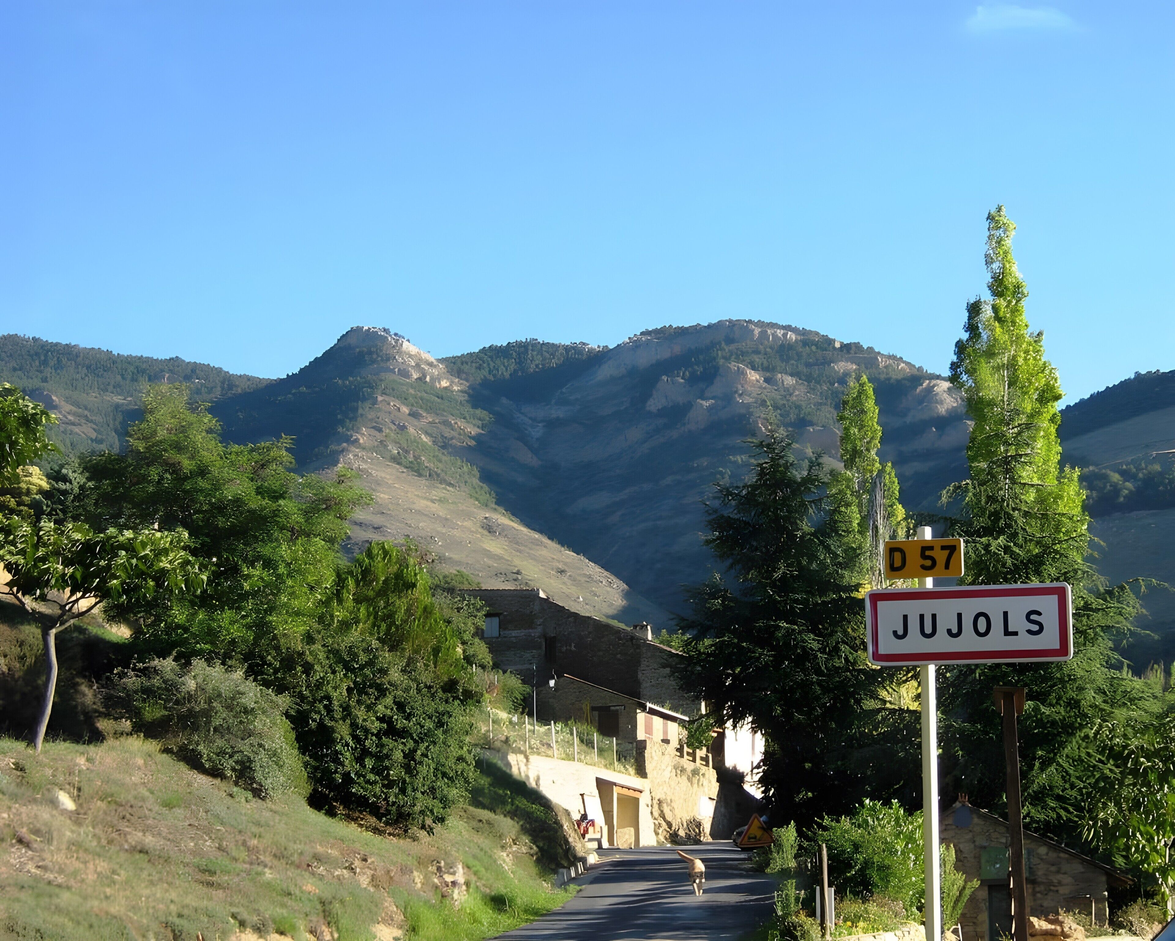 Una carretera rural con un cartel que indica 'Jujols' y un paisaje de montañas al fondo.